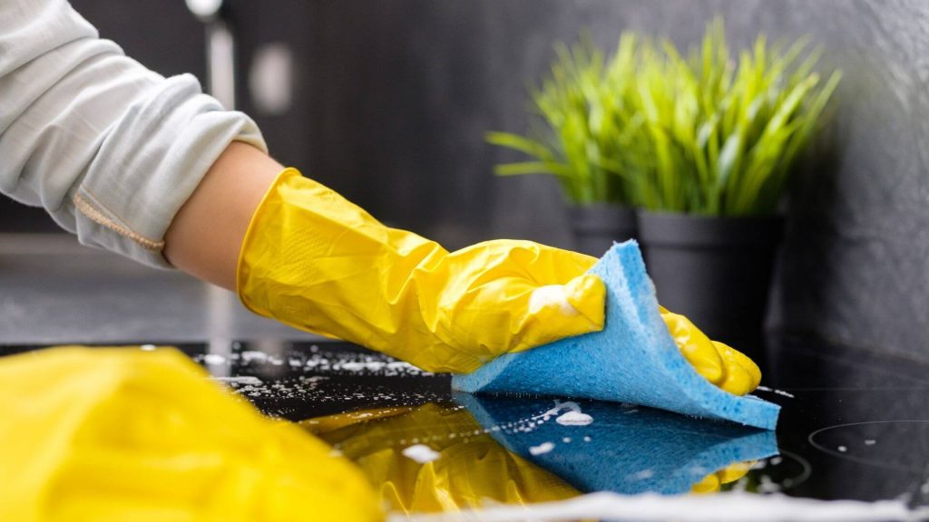 two hands wearing yellow gloves wiping and cleaning a table surface